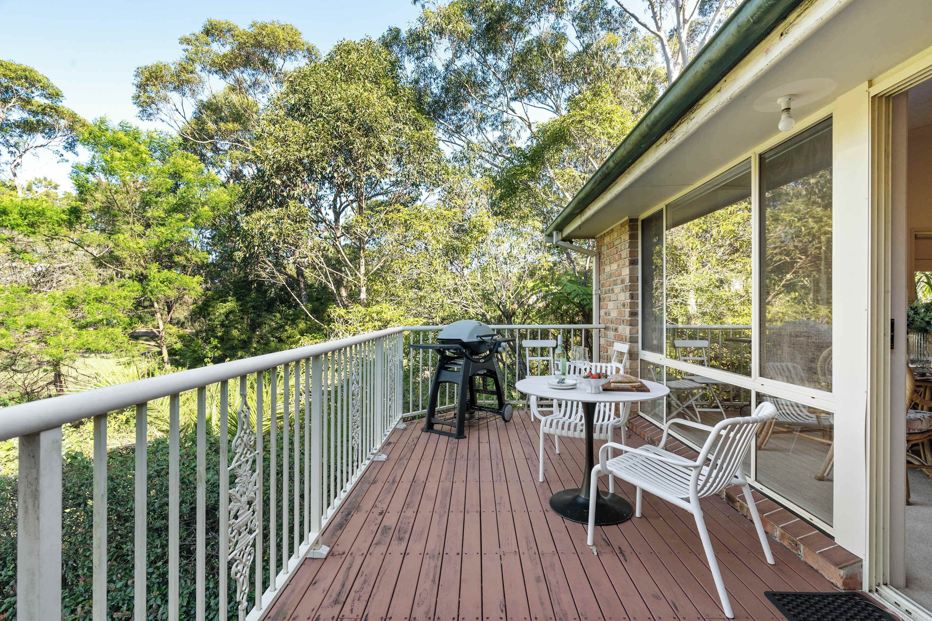 A wooden deck with a grill, white chairs, and a table.