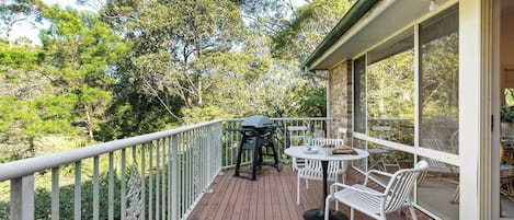 A wooden deck with a grill, white chairs, and a table.