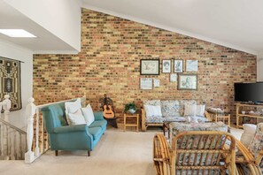 Ein Wohnzimmer mit Backsteinwand, einem blauen Sofa, einem Korbstuhl, einer Gitarre und einem Fernseher.