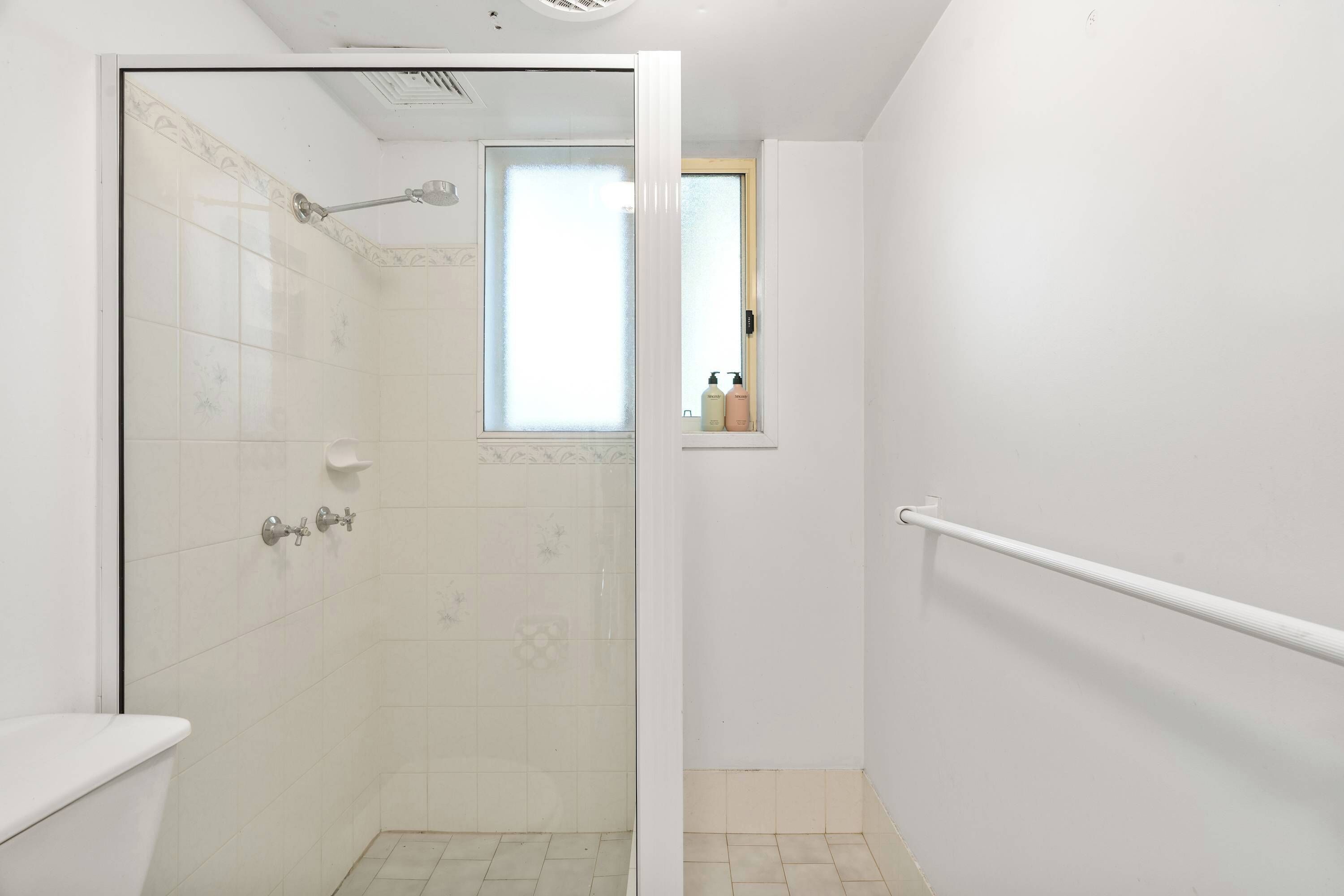 A bathroom with a shower, toilet, and window.