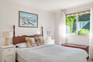 Ein Schlafzimmer mit einem Bett, einem Nachttisch, Vorhängen an einem Fenster und einem Bild an der Wand.