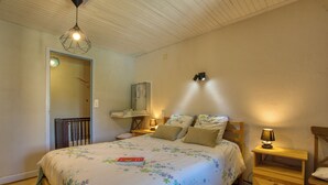 Un dormitorio con cama, mesitas de noche, lámpara colgante y estante en la pared.