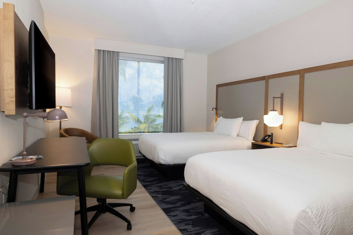 A hotel room with two beds, a desk, a chair, a TV, and a window with curtains.