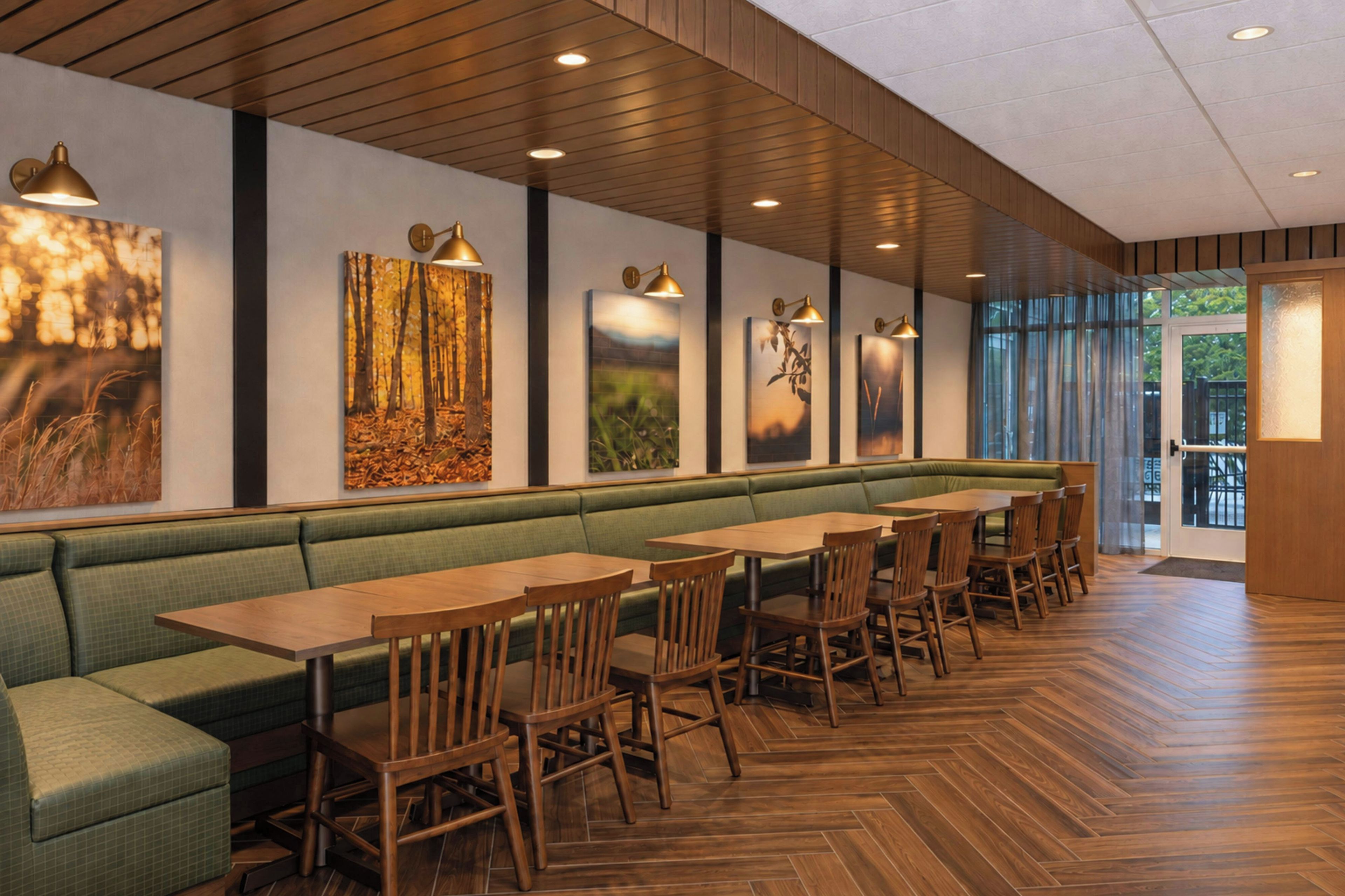 Un restaurante con suelo de madera, asientos acolchados verdes y luces colgantes fijadas a la pared.