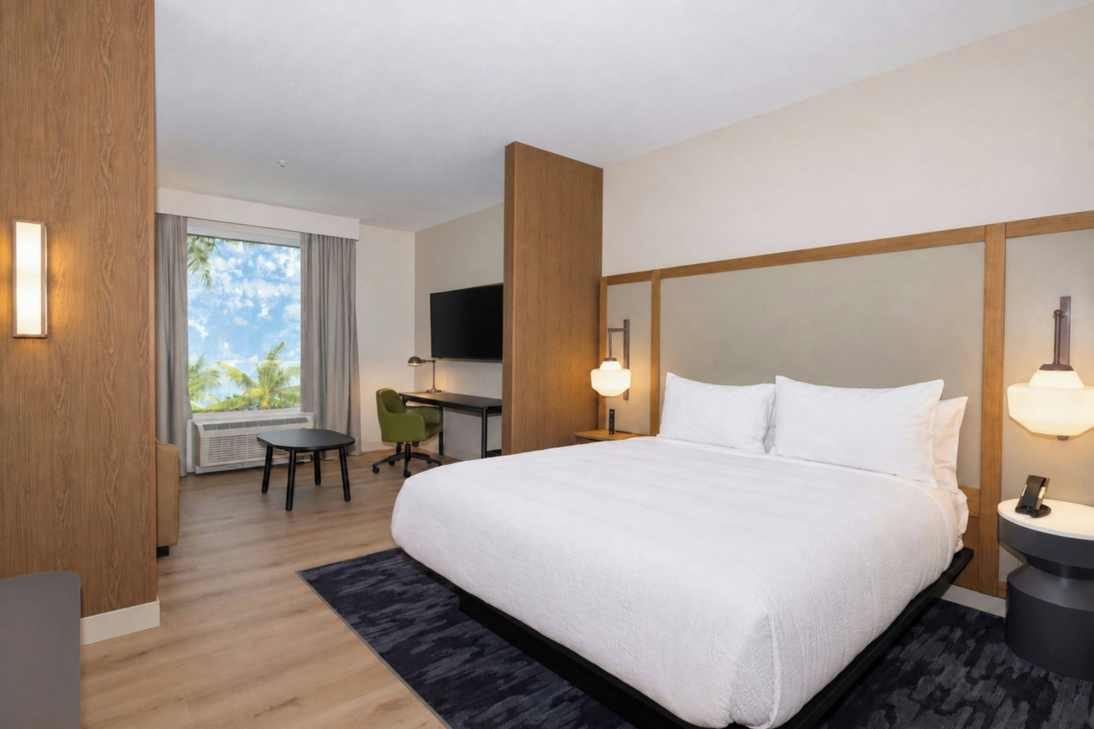 Habitación de hotel con una cama grande, un escritorio, una silla, un televisor y vistas al exterior.
