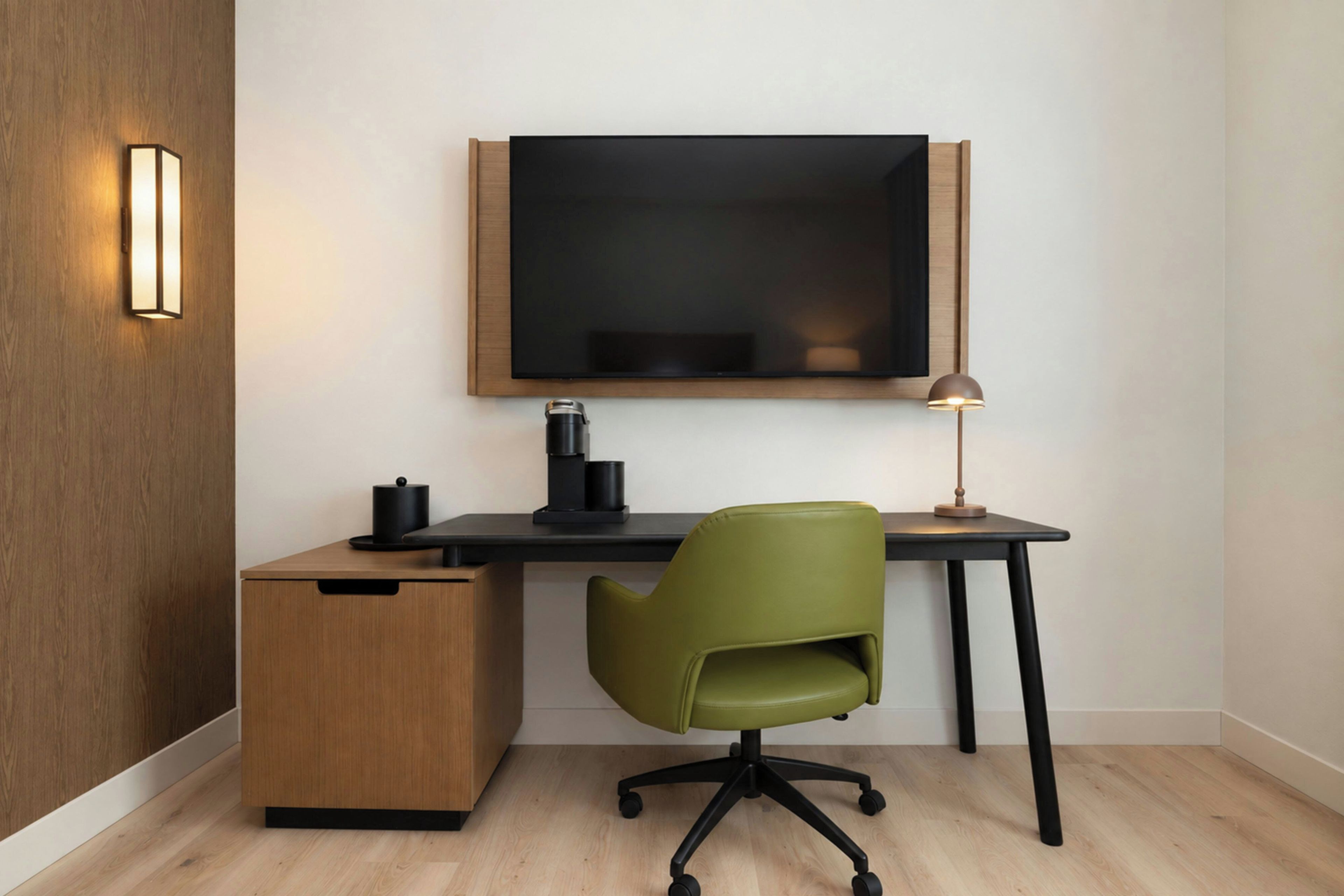 A modern office space with a wooden desk, a green office chair, a black monitor, and a lamp.