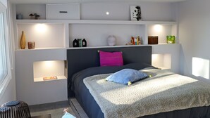A bedroom with a bed, bedside tables, shelves with items, and a window.