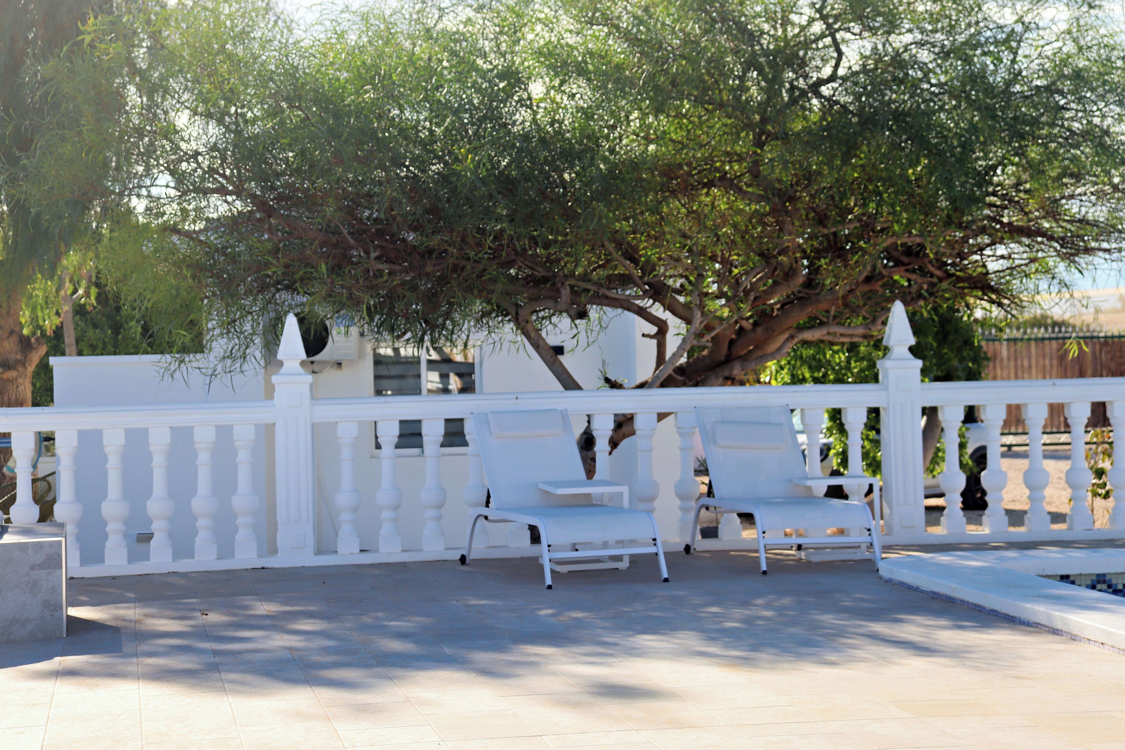 Un espace extérieur aménagé avec des sièges blancs, une clôture blanche, un arbre et un banc.