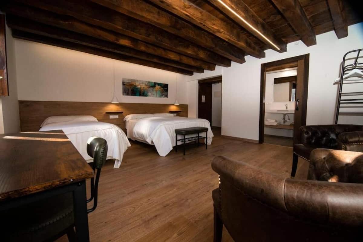 Habitación de hotel con dos camas, techo de madera, escritorio, silla y espejo.