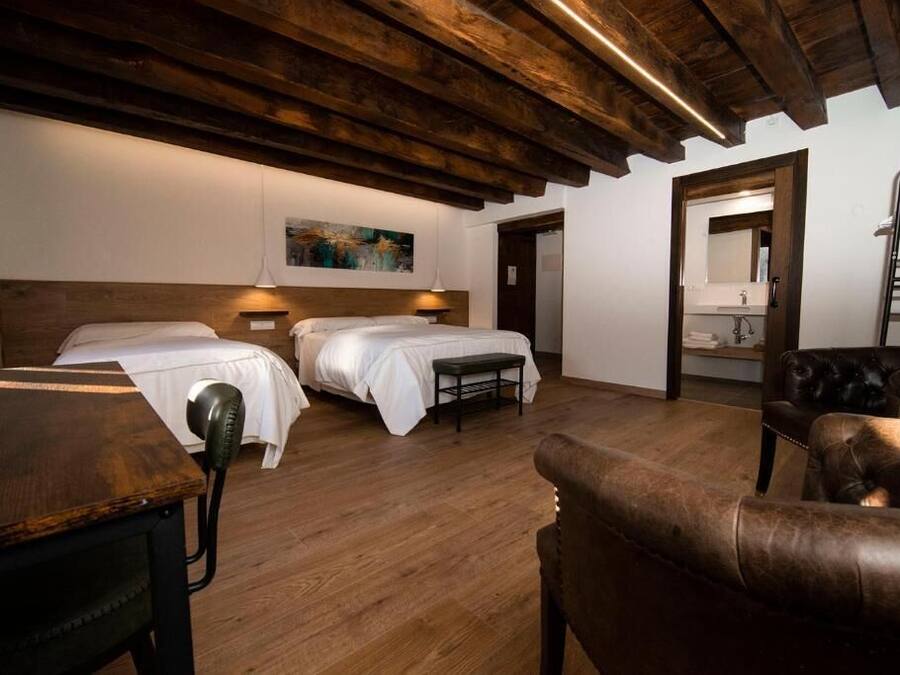 Ein Hotelzimmer mit zwei Betten, einer Holzbalkendecke, einem Schreibtisch, einem Stuhl und einem Spiegel.