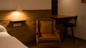 Una habitación con cabecera de madera, una silla de madera, una mesita pequeña y una lámpara colgante blanca.