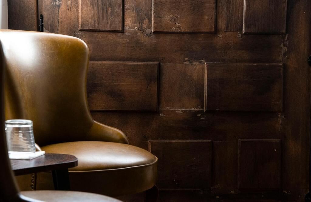 A leather chair and a table with a glass, against a wooden wall.