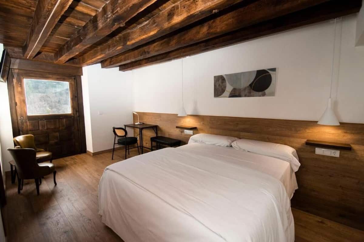 Un dormitorio con techo de madera, una cama, un escritorio, una silla y un ventanal.
