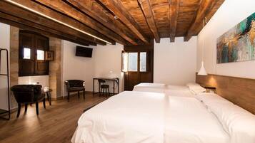 A hotel room with a wooden ceiling, two beds, a desk, and chairs.