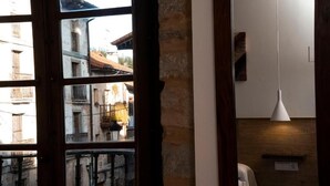 Una habitación con un ventanal grande, pared de madera, lámpara colgante y un estante pequeño.