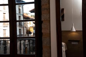 A room with a large window, a wooden wall, a hanging light fixture, and a small shelf.