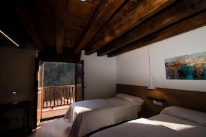 A room with two beds, a wooden ceiling, a painting on the wall, and a balcony with a view.