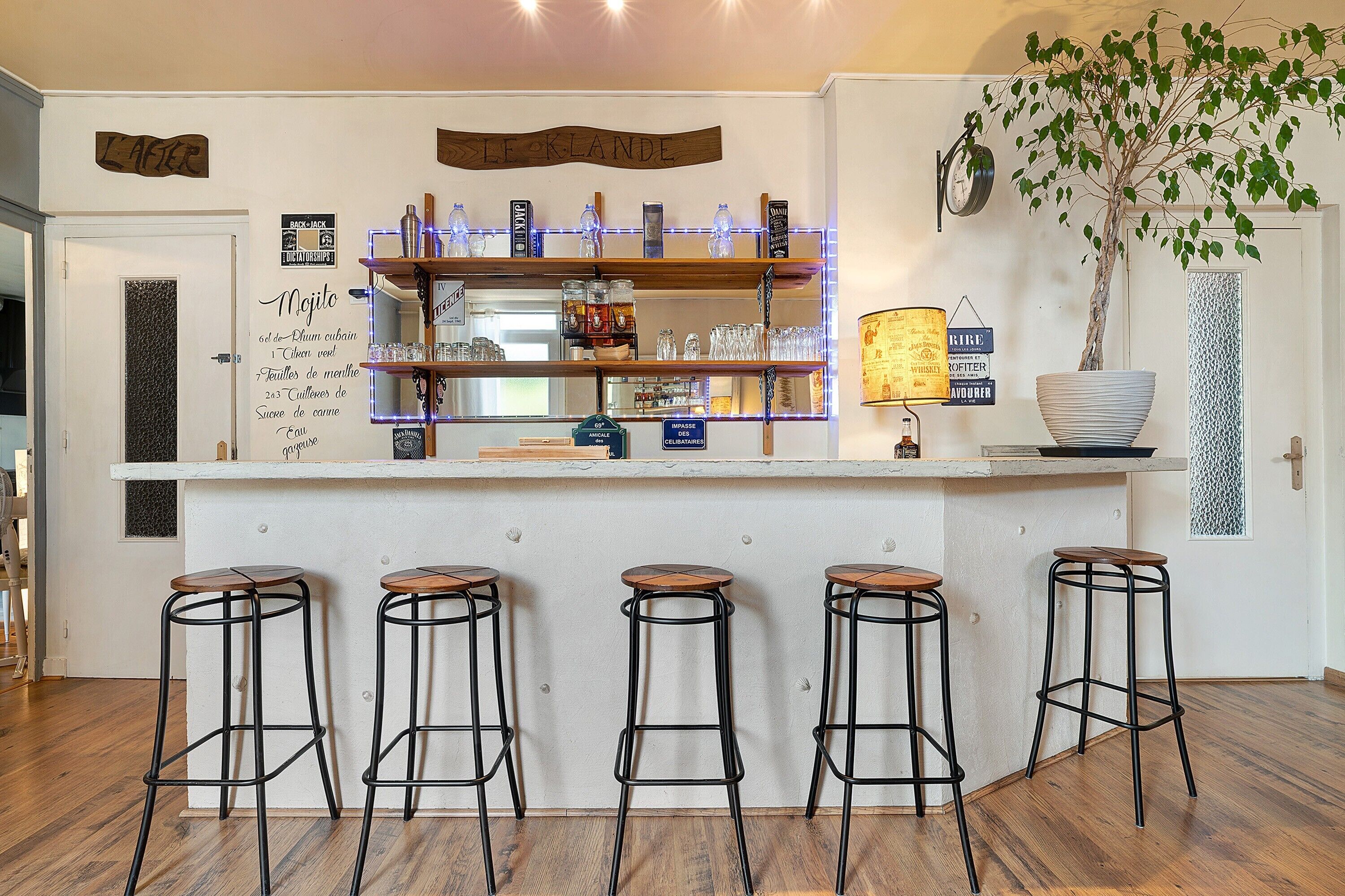 A bar area with stools, shelves with bottles, a potted plant, and a sign reading 'LE ORLANDE'.