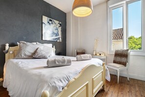 Een slaapkamer met een bed, een stoel, een nachtkastje, een lamp en een raam met uitzicht.