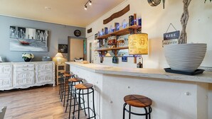 Un espace bar avec des tabourets, des étagères remplies de bouteilles, une horloge et un tableau accroché au mur.