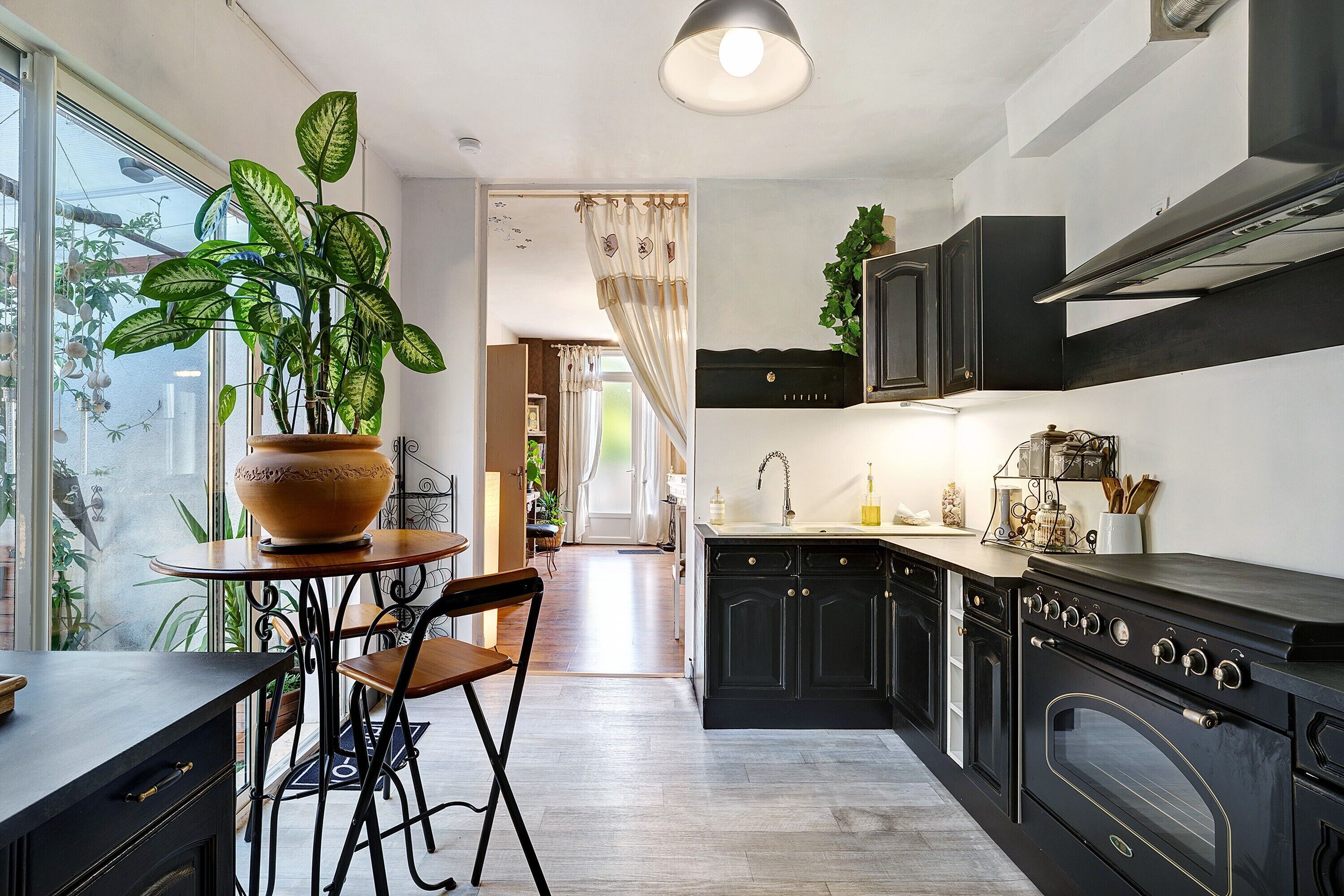 A modern kitchen with dark cabinetry, a large stove, and a potted plant on a table.