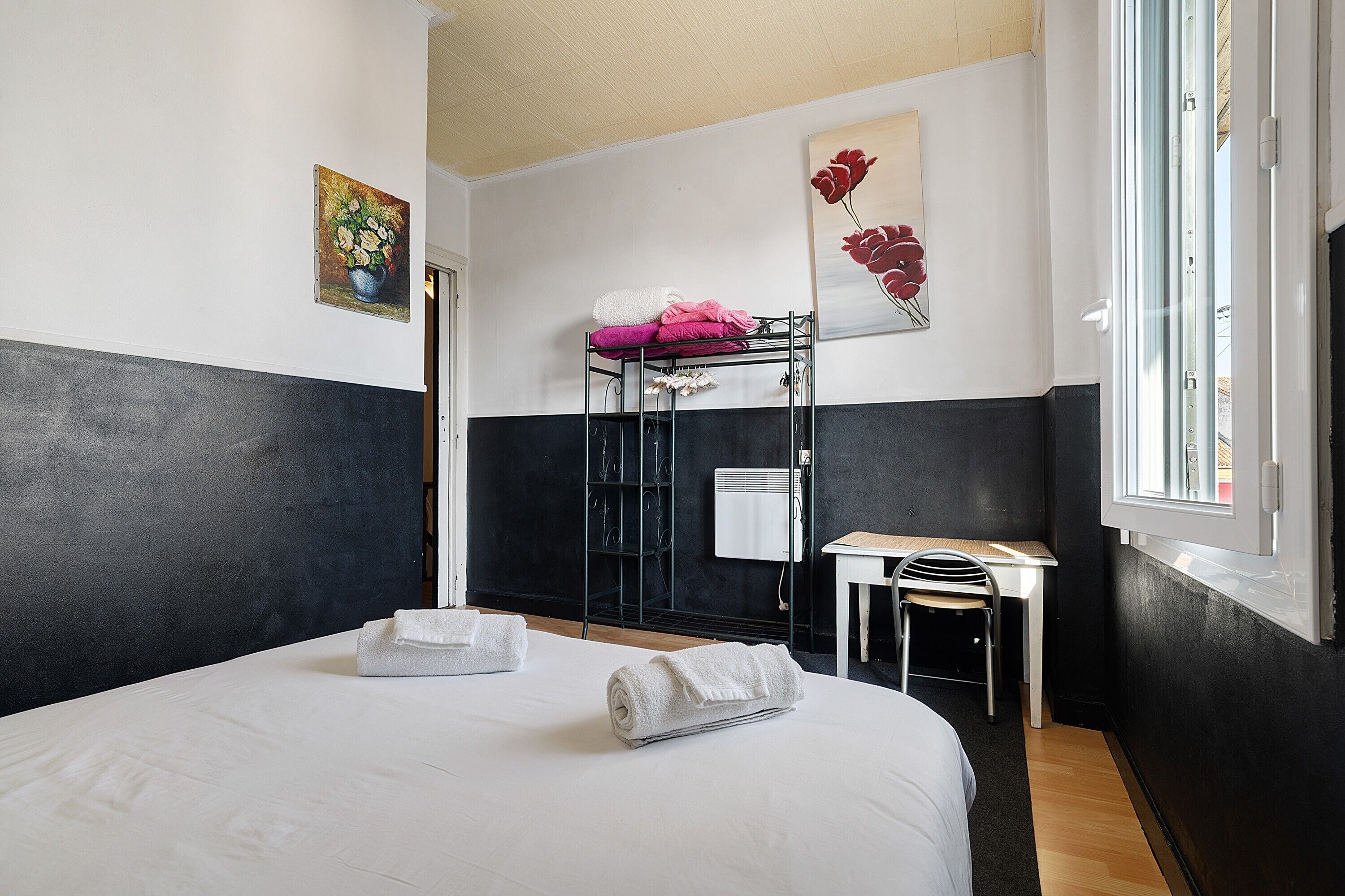 Habitación de hotel con cama, escritorio, silla, radiador y obras de arte en las paredes.