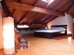 A loft bedroom with exposed wooden beams, a bed, a piano, and a standing lamp. - Farmhouse with garden, parking and fitness area near Bologna center (Bologna, Emilia-Romagna)
