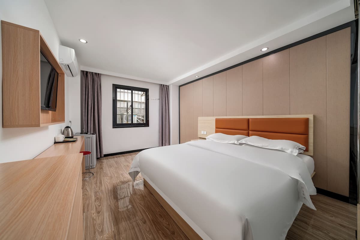 Una habitación de hotel moderna con una cama grande, un escritorio de madera, un televisor y una ventana con cortinas.