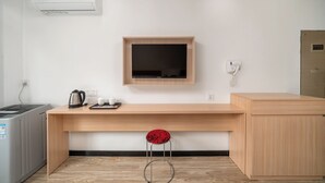 Una habitación de hotel moderna con un escritorio de madera, un televisor montado en la pared, un hervidor, tazas y un teléfono.