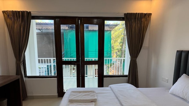 A hotel room with a large bed, a desk, and a view through a glass door. - Bougain villa (Canacona)