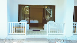A hotel room with a bed, a small table, and a chair. There is a balcony with a railing and a view of the outside. - Bougain villa (Canacona)