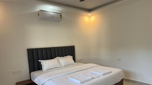 A modern hotel room with a large bed, a built-in nightstand, a ceiling fan, and an air conditioning unit. - Bougain villa (Canacona)