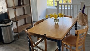 Un'area pranzo con un tavolo di legno, sedie, un vaso con fiori, una libreria e una finestra vista alberi.