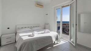 A bedroom with a bed, a nightstand, a radiator, and a sliding glass door leading to a balcony. - Hostdomus - Turtle House (Borgio)