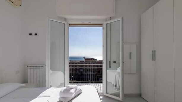 A bedroom with a bed, a white wardrobe, and a balcony with a view. - Hostdomus - Turtle House (Borgio)