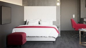 Una habitación de hotel moderna con una cama grande, un sillón rojo, un escritorio y un televisor montado en la pared.