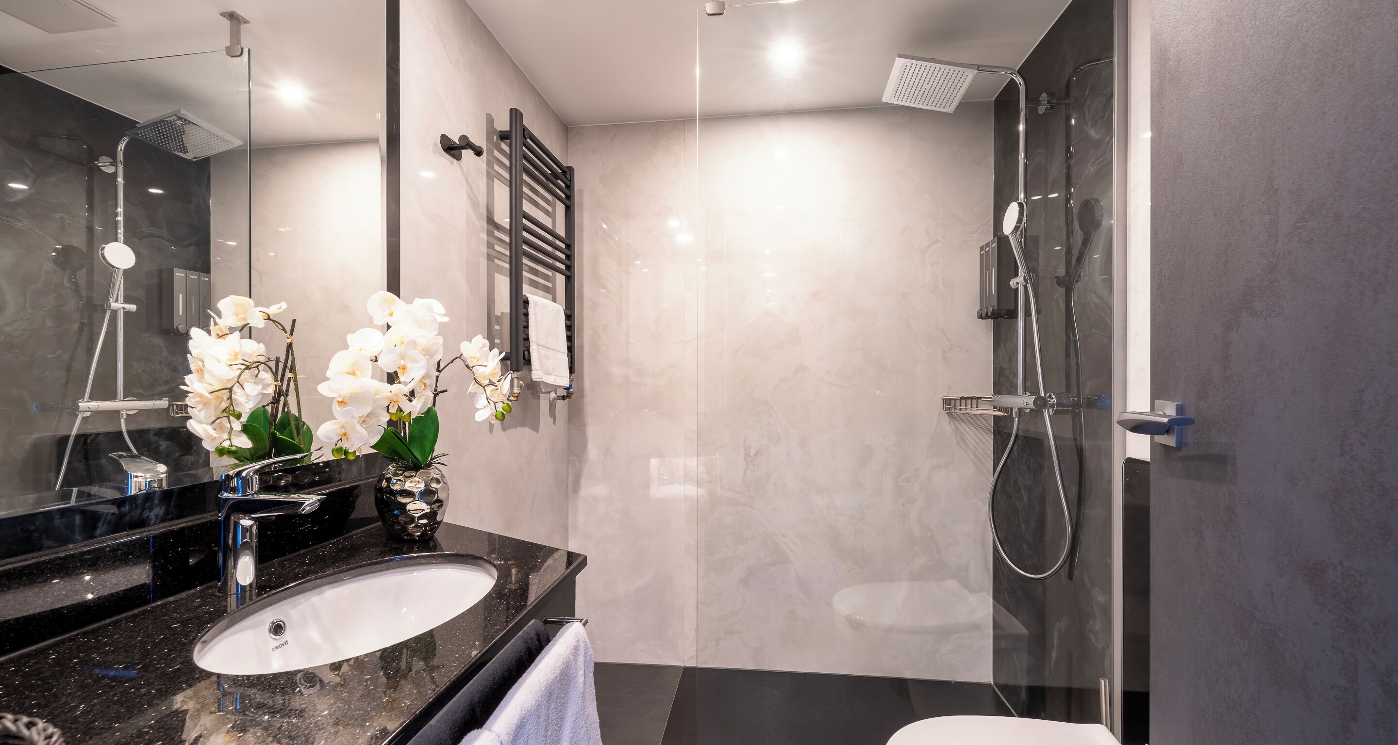 Ein modernes Badezimmer mit einer gläsernen Dusche, einem schwarzen Marmorwaschbecken und weißen Orchideen.