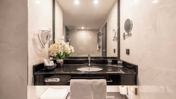 A modern bathroom with a black marble sink, a mirror, a towel rack, and a vase of white flowers.