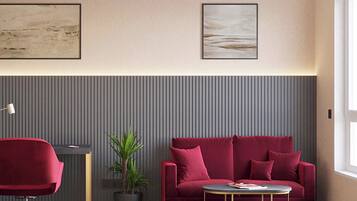 Ein modernes Zimmer mit einem roten Sofa, einem kleinen runden Tisch, einem roten Bürostuhl, einer Topfpflanze und zwei gerahmten Kunstwerken an der Wand.
