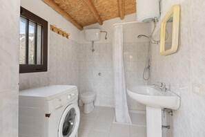 Casa de banho compacta com máquina de lavar, sanita, chuveiro e lavatório.