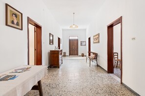 Um corredor com uma porta de madeira no final, uma mesa com revistas, um penteado e uma cadeira.