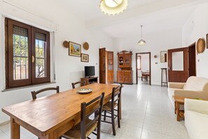 Uma sala de jantar com uma mesa e cadeiras de madeira, uma televisão e um armário.