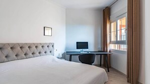Et hotelværelse med en stor seng, et skrivebord med en computer og et vindue med gardiner.