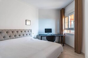 A hotel room with a large bed, a desk with a computer, and a window with curtains. - Casa Arte-Luxury Apartments Islantilla-RuitenAppartementen (Lepe)