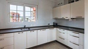 Et moderne køkken med hvide skabe, en sort bordplade og et vindue med udsigt til bygninger.