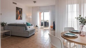 A modern living room with a sofa, a dining table with chairs, and a view to the outside. - Casa Mar-Luxury Apartments Islantilla-RuitenAppartementen (Lepe)