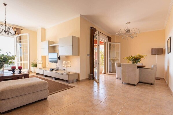 A modern living room with a sofa, a TV, a dining table, and a chandelier. - Casa GVista-Luxury Apartments Islantilla-RuitenAppartementen (Lepe)