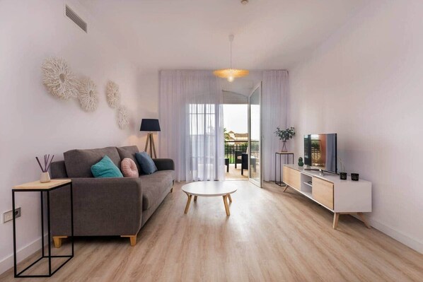 A modern living room with a sofa, coffee table, TV, and a balcony view. - Casa Loft-Luxury Apartments Islantilla-RuitenAppartementen (Lepe)