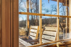 A wooden-framed window with a view of a wooden deck and chairs outside.