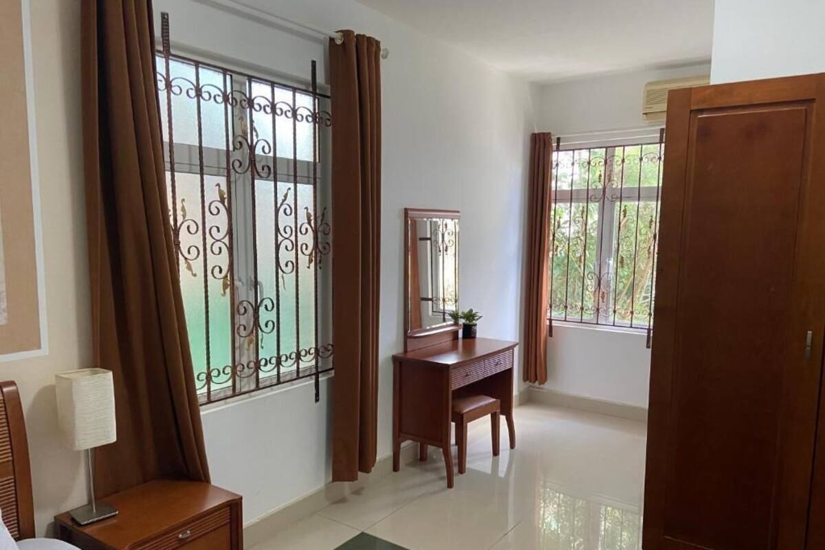 A bedroom with a bed, a nightstand, a desk, a mirror, and two windows with curtains.